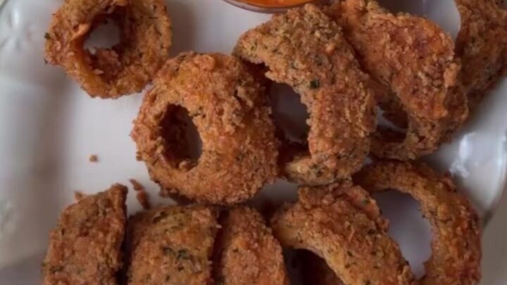 Crispy golden onion rings piled on a platter with a bowl of spicy remoulade sauce