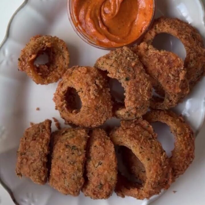 Crispy golden onion rings piled on a platter with a bowl of spicy remoulade sauce