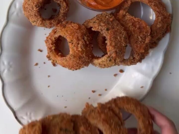 Crispy golden onion rings piled high with a bowl of garlic herb aioli