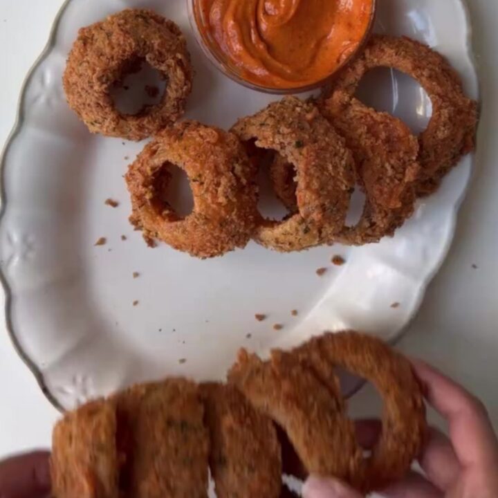 Crispy golden onion rings piled high with a bowl of garlic herb aioli