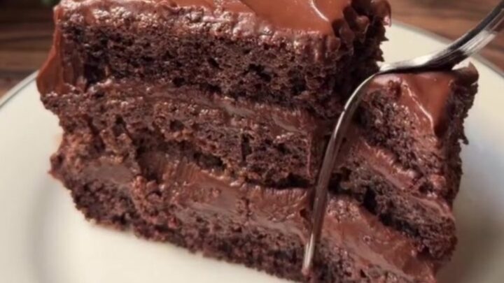 A slice of no-bake chocolate mousse cake with a thick cocoa dusting on top, showing the creamy interior and biscuit base.