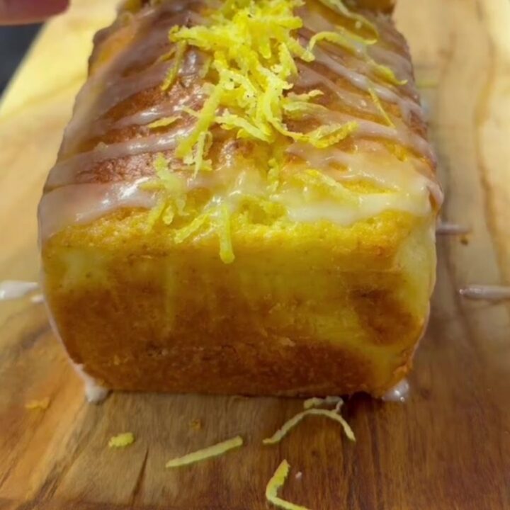 Moist lemon pound cake with glossy white glaze, sliced on a wooden board