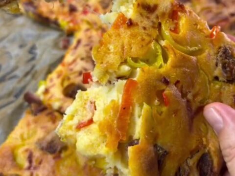 Sliced crepe party squares with melted cheese, sucuk, corn, and peppers on a parchment-lined baking sheet.