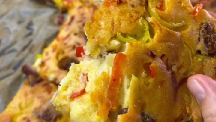 Sliced crepe party squares with melted cheese, sucuk, corn, and peppers on a parchment-lined baking sheet.