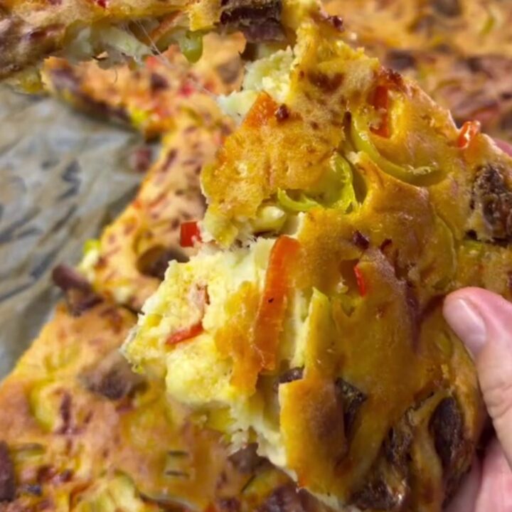 Sliced crepe party squares with melted cheese, sucuk, corn, and peppers on a parchment-lined baking sheet.