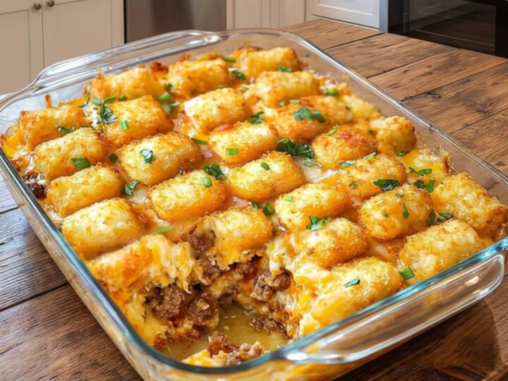 A steaming portion of cheesy tater tot beef casserole being lifted from a glass dish with a spatula.