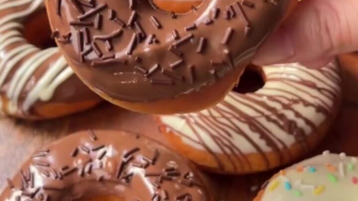 A stack of golden fried donuts dipped in milk chocolate and drizzled with white chocolate
