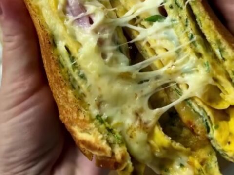 Crispy egg-dipped ham and cheese toastie sliced in half showing melted cheese pull