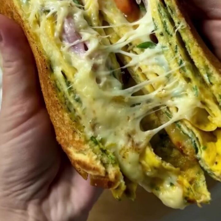 Crispy egg-dipped ham and cheese toastie sliced in half showing melted cheese pull