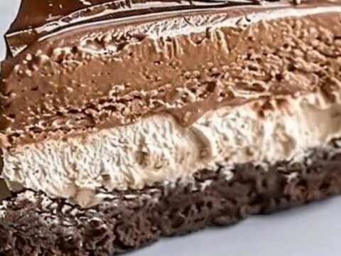 A slice of triple chocolate mousse cake with piped rosettes on a white plate.