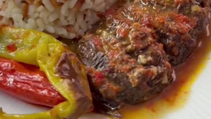 Roasted accordion eggplant stuffed with beef, peppers, and tomatoes in a baking dish.