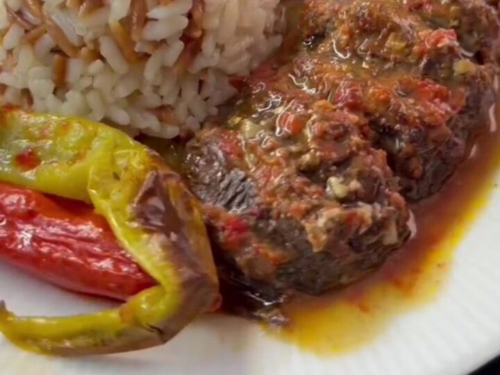 Roasted accordion eggplant stuffed with beef, peppers, and tomatoes in a baking dish.