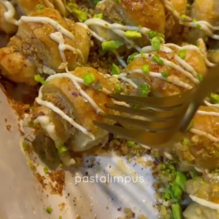 Golden puff pastry mini baklava rolls dusted with powdered sugar on a baking sheet.