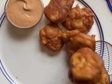 Crispy golden chicken nuggets piled in a basket with fries and Texas toast, with a cup of creamy pepper sauce for dipping.