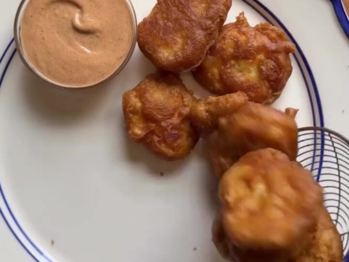 Crispy golden chicken nuggets piled in a basket with fries and Texas toast, with a cup of creamy pepper sauce for dipping.