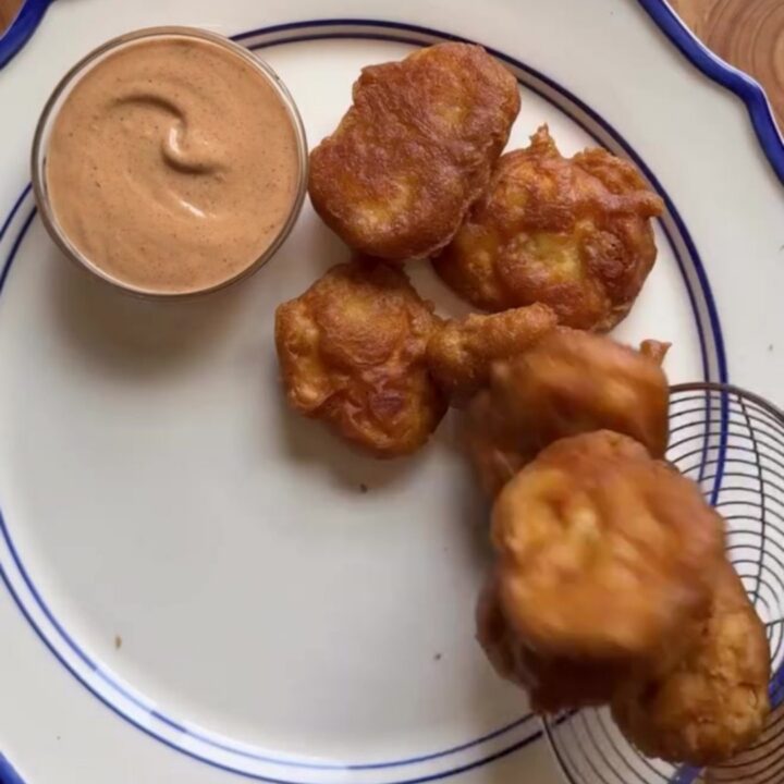 Crispy golden chicken nuggets piled in a basket with fries and Texas toast, with a cup of creamy pepper sauce for dipping.