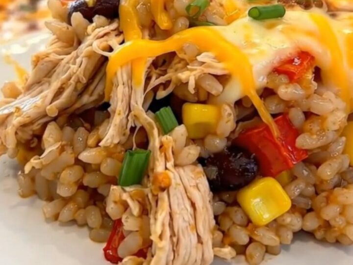 A serving of Southwest chicken casserole on a white plate, showing melted cheddar cheese, rice, beans, and corn.