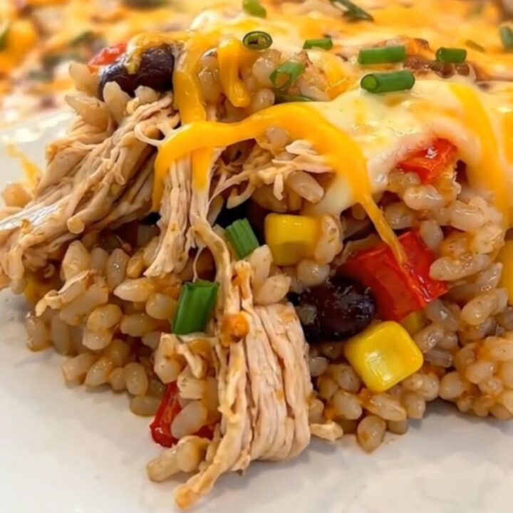 A serving of Southwest chicken casserole on a white plate, showing melted cheddar cheese, rice, beans, and corn.