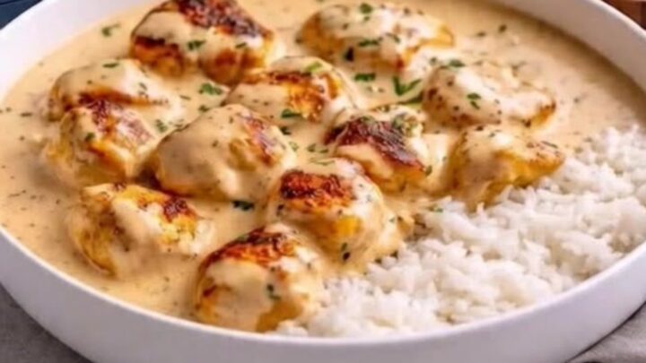 A wide white bowl featuring golden seared chicken pieces in a creamy garlic parmesan sauce served over fluffy white rice.