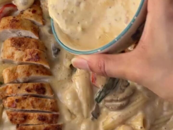 A creamy rigatoni pasta with sun-dried tomatoes, sliced chicken, and fresh basil in a skillet