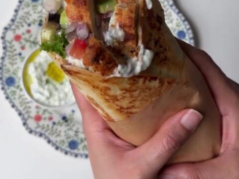 Sliced Greek chicken wrap showing layers of charred chicken, romaine, tomatoes, and tzatziki in a warm tortilla.