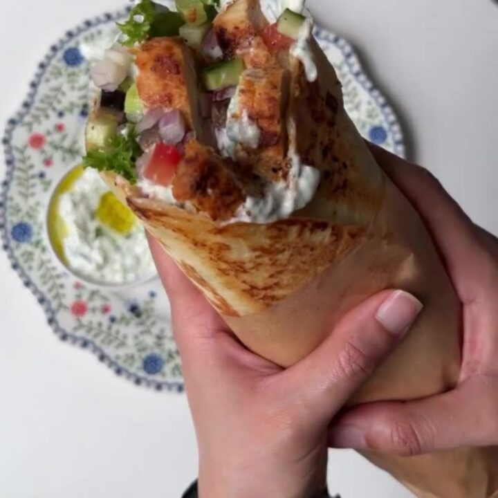 Sliced Greek chicken wrap showing layers of charred chicken, romaine, tomatoes, and tzatziki in a warm tortilla.