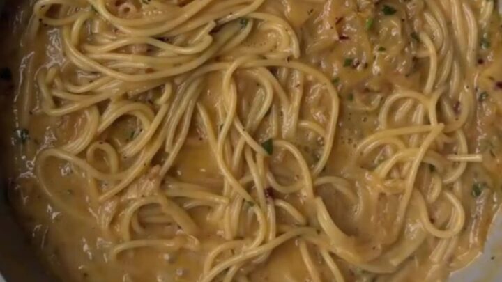 Twirled fettuccine with caramelized onions on a rustic ceramic plate, topped with shaved Parmesan