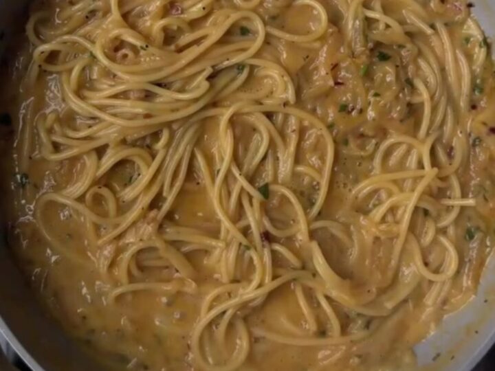 Twirled fettuccine with caramelized onions on a rustic ceramic plate, topped with shaved Parmesan