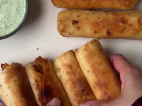 Crispy golden chicken taquitos arranged on a platter with a bowl of vibrant green crema for dipping