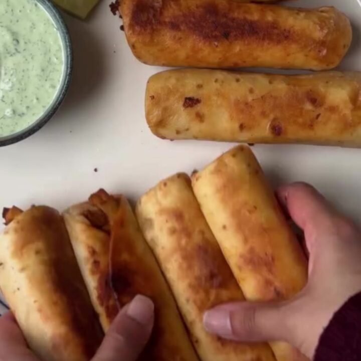 Crispy golden chicken taquitos arranged on a platter with a bowl of vibrant green crema for dipping