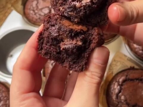 Hands breaking a warm brownie muffin in half, showing the fudgy center oozing