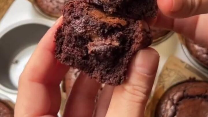 Hands breaking a warm brownie muffin in half, showing the fudgy center oozing