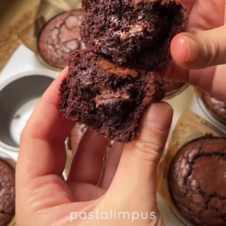 Hands breaking a warm brownie muffin in half, showing the fudgy center oozing