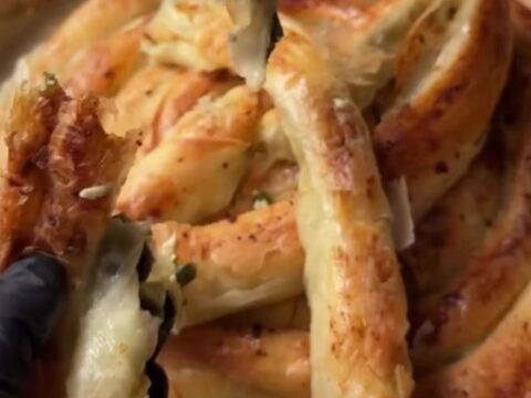 Slicing a golden twisted börek with a chef's knife, showing crisp layers and spinach-feta filling