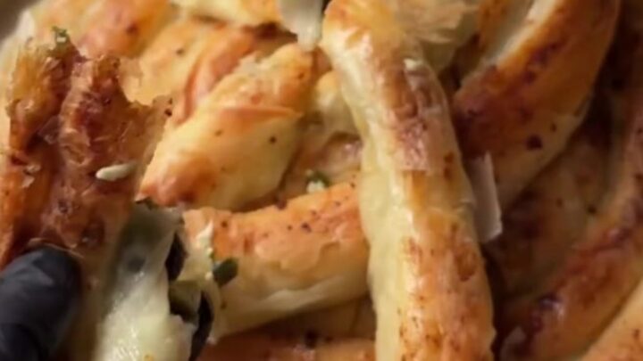 Slicing a golden twisted börek with a chef's knife, showing crisp layers and spinach-feta filling