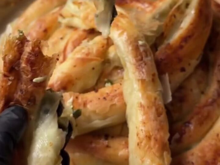 Slicing a golden twisted börek with a chef's knife, showing crisp layers and spinach-feta filling