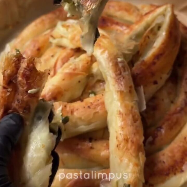 Slicing a golden twisted börek with a chef's knife, showing crisp layers and spinach-feta filling