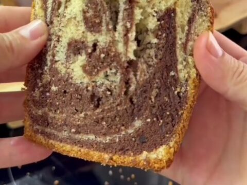 Marble swirl loaf cake with cocoa ribbons and roasted hazelnuts on a wooden board, sliced to show the interior