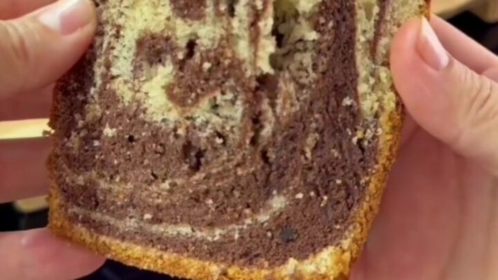 Marble swirl loaf cake with cocoa ribbons and roasted hazelnuts on a wooden board, sliced to show the interior