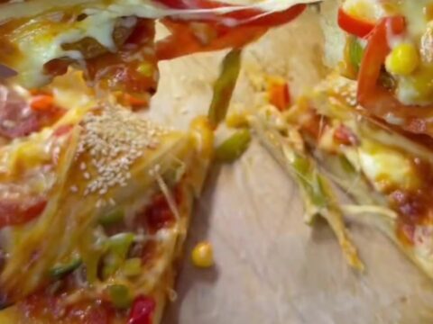 Golden sesame-crusted crown pizza ring on a baking sheet, with melted cheese visible in the folds.