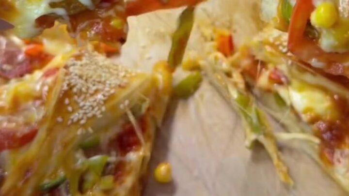 Golden sesame-crusted crown pizza ring on a baking sheet, with melted cheese visible in the folds.