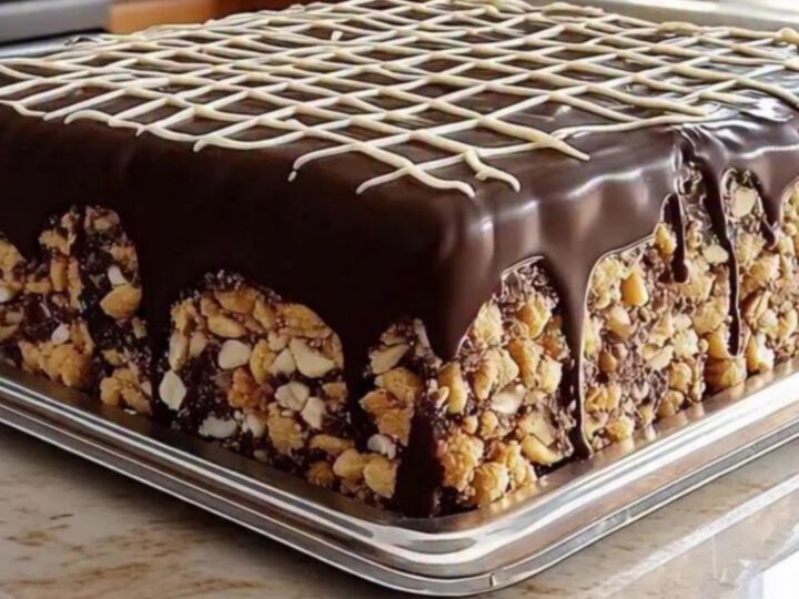 A square chocolate biscuit cake with a glossy dark chocolate glaze and white chocolate drizzle on a silver tray.