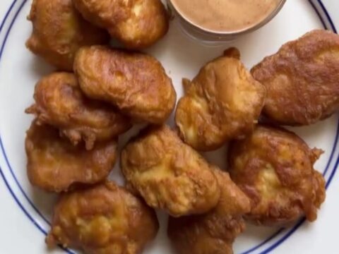 Golden crispy chicken nuggets piled on a plate with a bowl of tangy cane sauce for dipping.