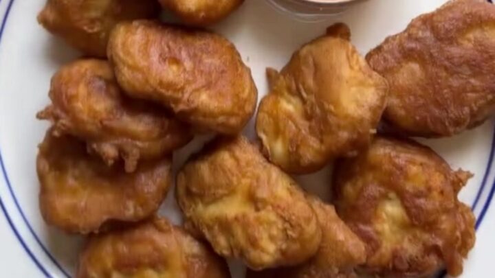Golden crispy chicken nuggets piled on a plate with a bowl of tangy cane sauce for dipping.