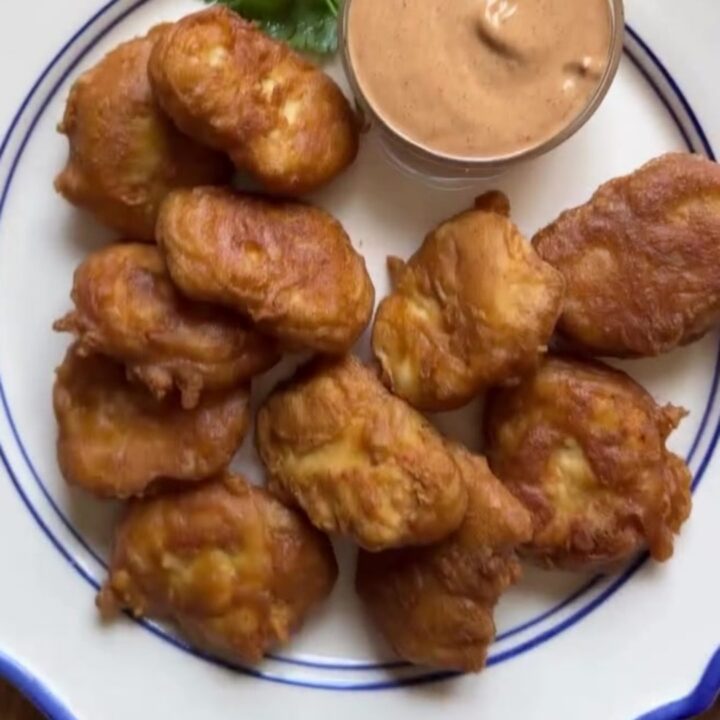 Golden crispy chicken nuggets piled on a plate with a bowl of tangy cane sauce for dipping.