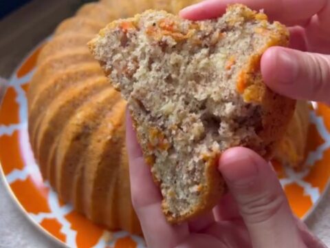 Spiced carrot walnut bundt cake inverted on a wooden board, showing fluted ridges and a slice with tender crumb.