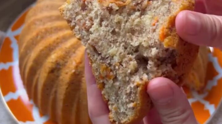 Spiced carrot walnut bundt cake inverted on a wooden board, showing fluted ridges and a slice with tender crumb.