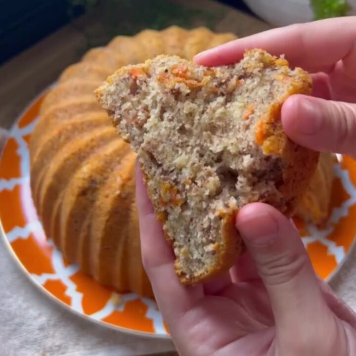 Spiced carrot walnut bundt cake inverted on a wooden board, showing fluted ridges and a slice with tender crumb.