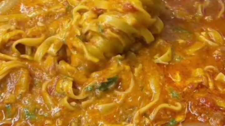 Twirled tagliatelle pasta with glossy vegetable sauce, garnished with parsley and Parmesan