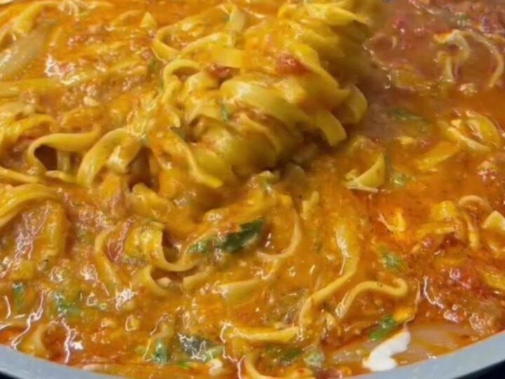 Twirled tagliatelle pasta with glossy vegetable sauce, garnished with parsley and Parmesan